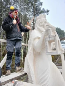 La Gardienne, sculpture monumentale de Raphaëlle Duval en pierre calcaire à Boscamnant, 2,50 m de hauteur, visible en extérieur, montrant l’artiste en train de sculpter.