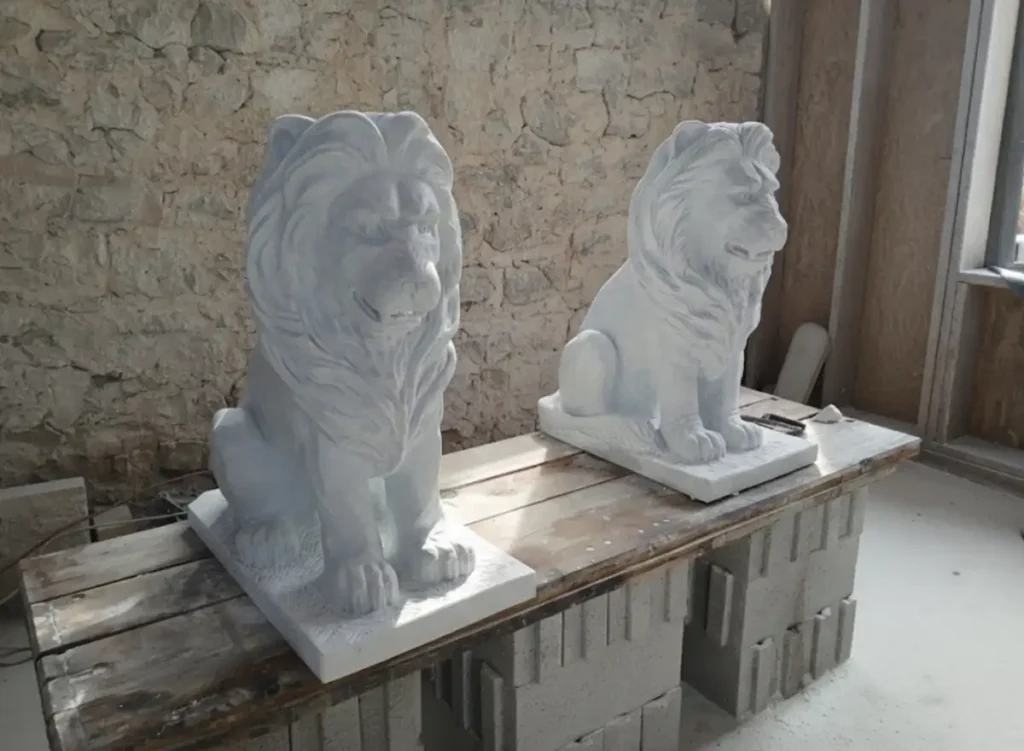 Deux sculptures en marbre de Carrare représentant des lions vues de face, réalisées par l’artiste Raphaëlle Duval, dimensions 80 × 70 × 40 cm.