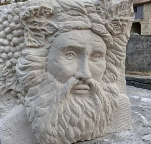 Bas-relief en pierre représentant Bacchus, visage barbu couronné de feuilles de vigne, réalisé par les élèves des Ateliers Raphaëlle à Bassens (33530)