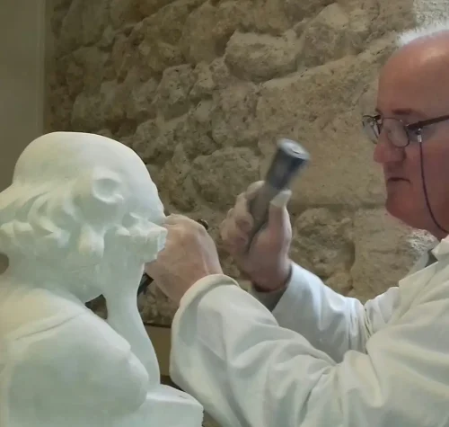 Élève des Ateliers Raphaëlle taillant un buste en pierre au maillet et au ciseau dans l'atelier de Bassens (33530)